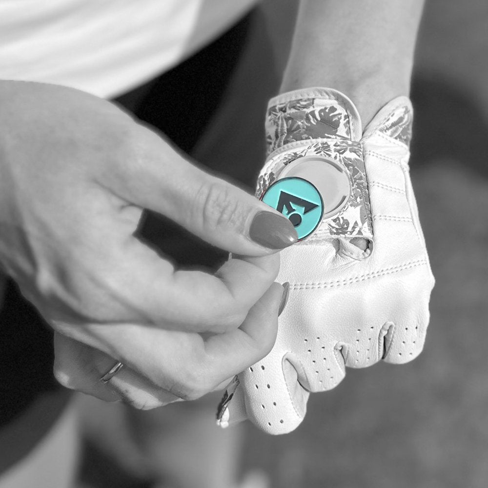 Close up of a woman's hand placing her magnetic ball marker on her golf glove with palm trees, everything in black and white.