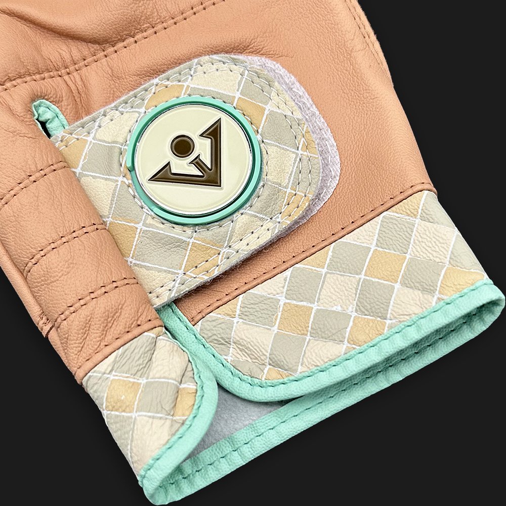 Brown golf glove with magnetic ball marker and checkered pattern, close up with dark background.