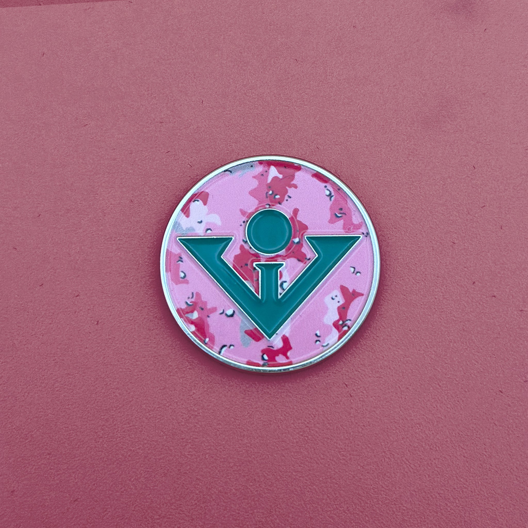 Pink camo with green logo magnetic golf ball marker and green background as backdrop.