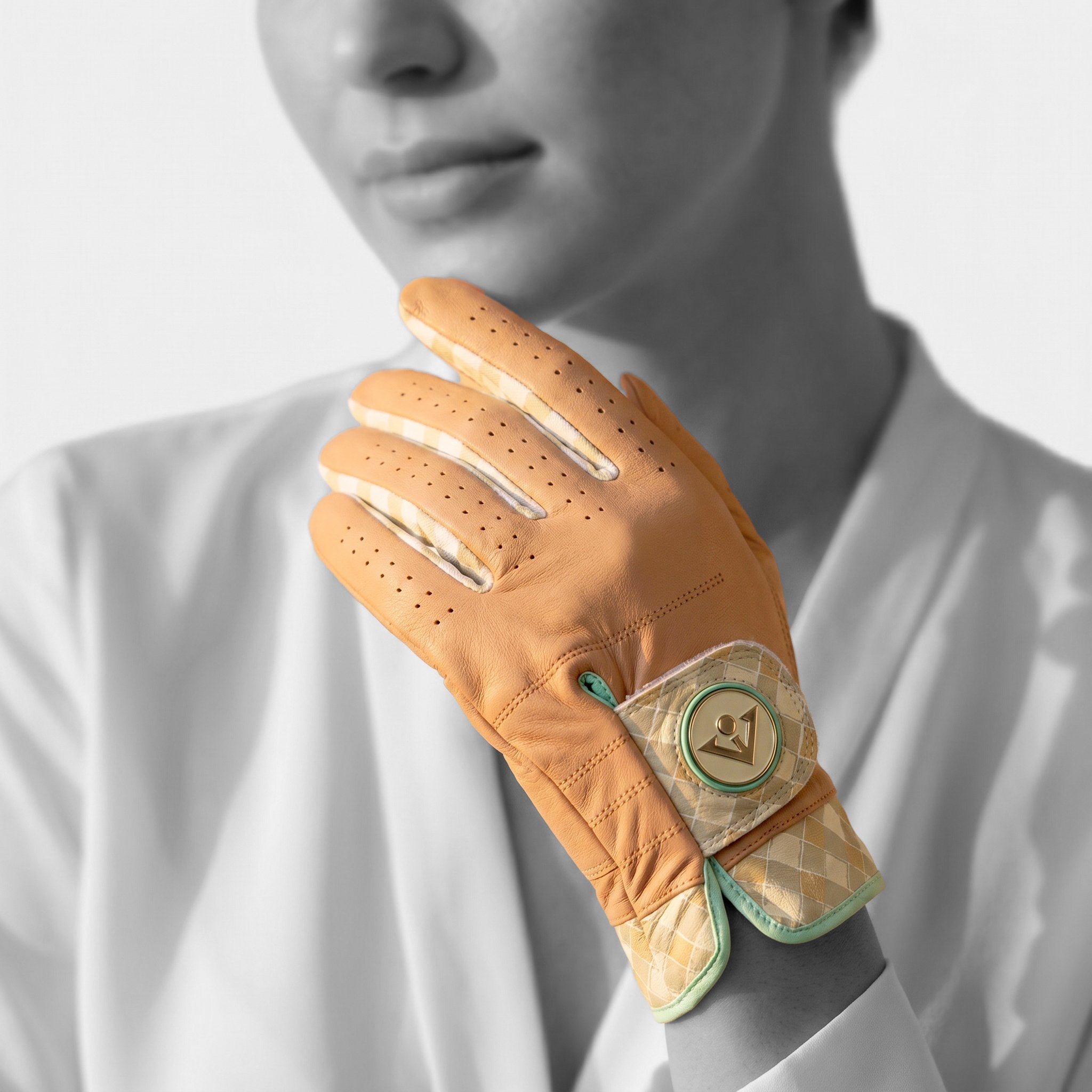Close-up of a woman wearing a designer tan leather golf glove with decorative elements on a light gray background
