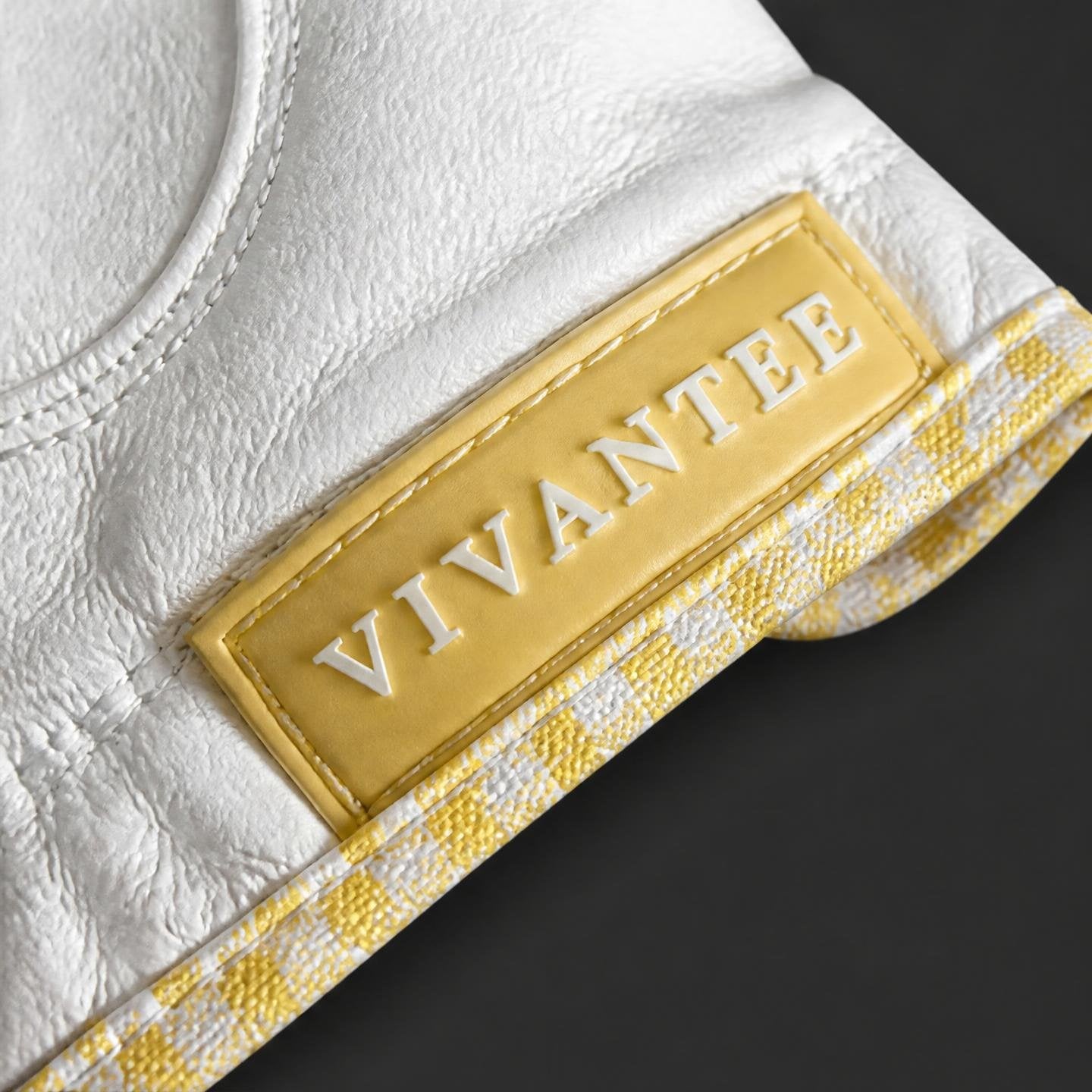 Close up of VivanTee Golf name tag in butter yellow on a golf glove and a black background.