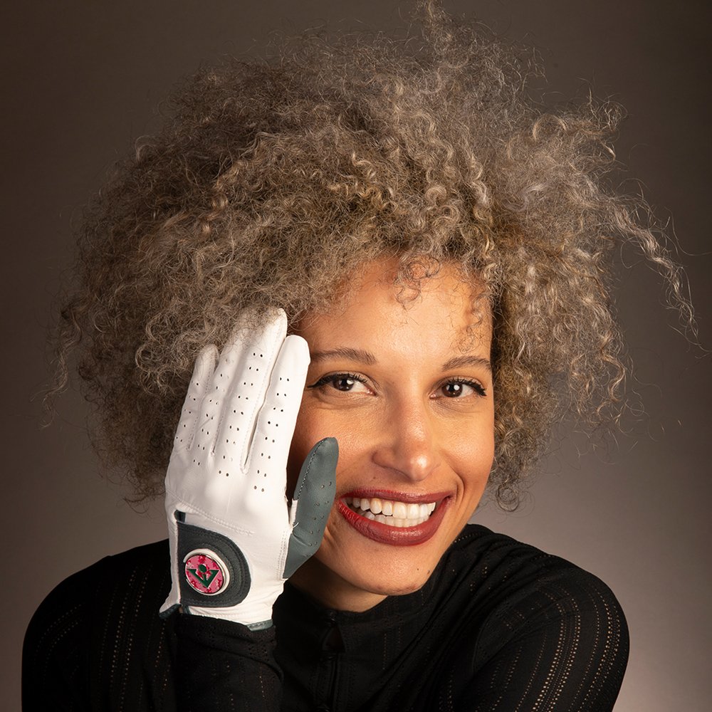 Woman with curly hair placing her hand on her cheek with a womans white and charcoal golf glove with pink magnetic ball marker.