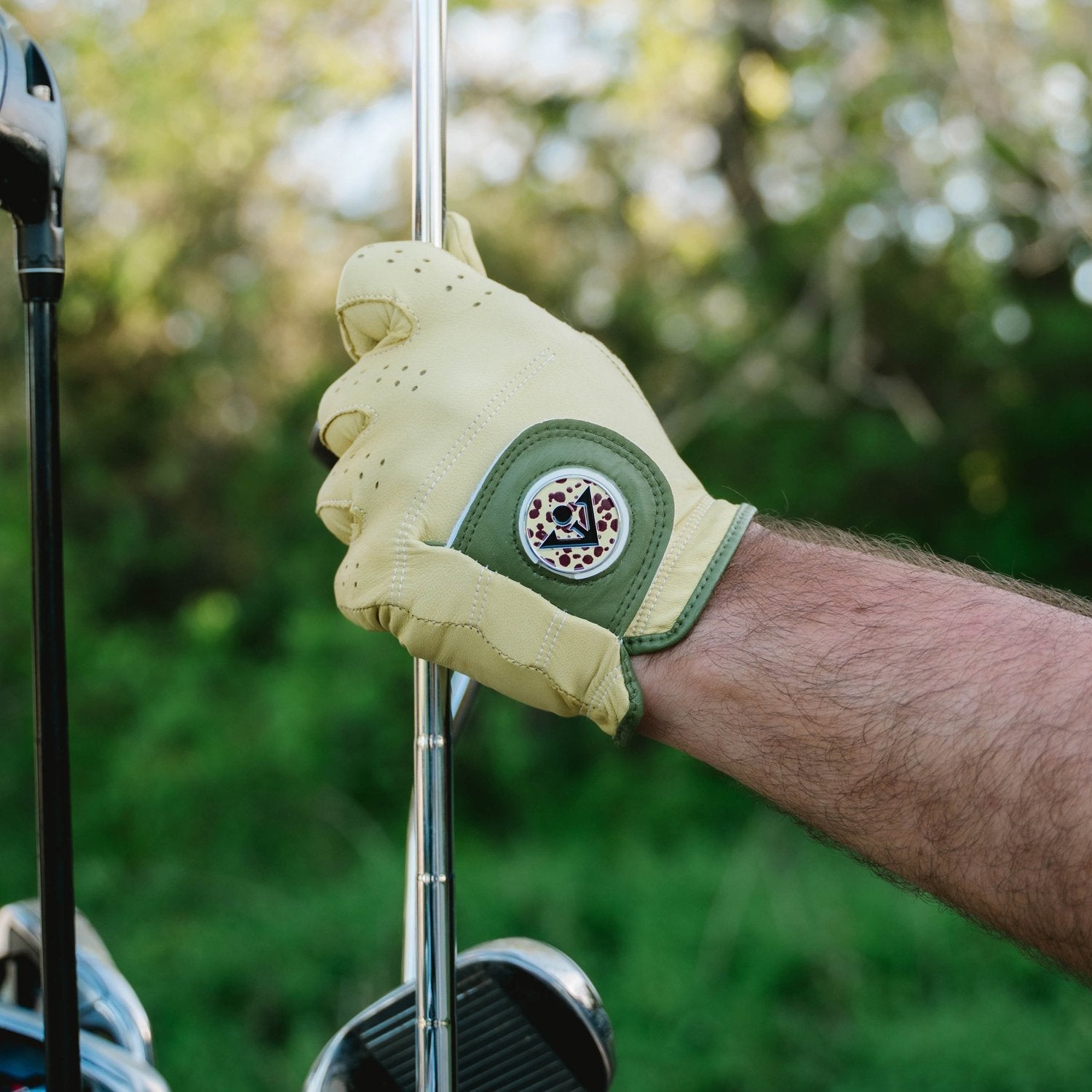 Men's yellow and green golf glove with a cheetah print magnetic ball marker putting away a golf club in their bag.
