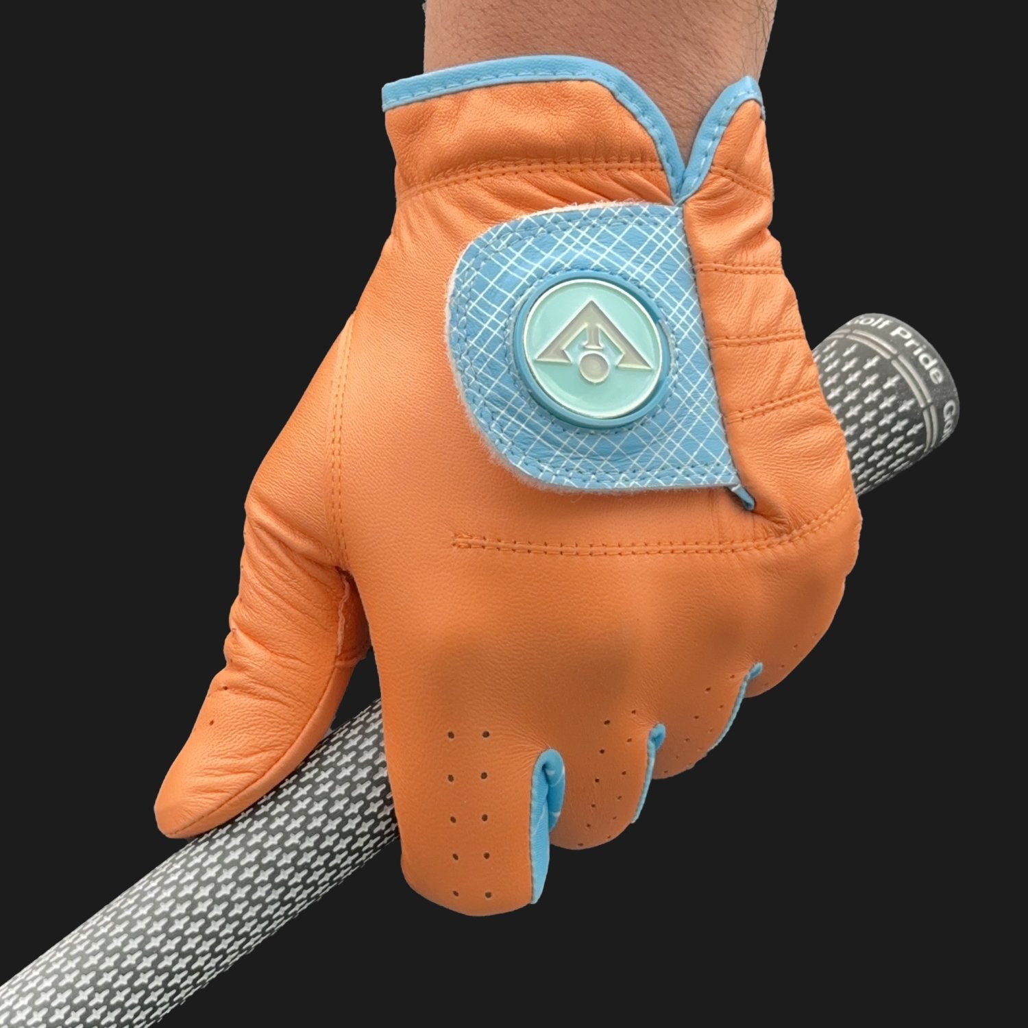 Orange golf glove with magnetic ball marker in blue, holding a golf club with a dark backdrog.  