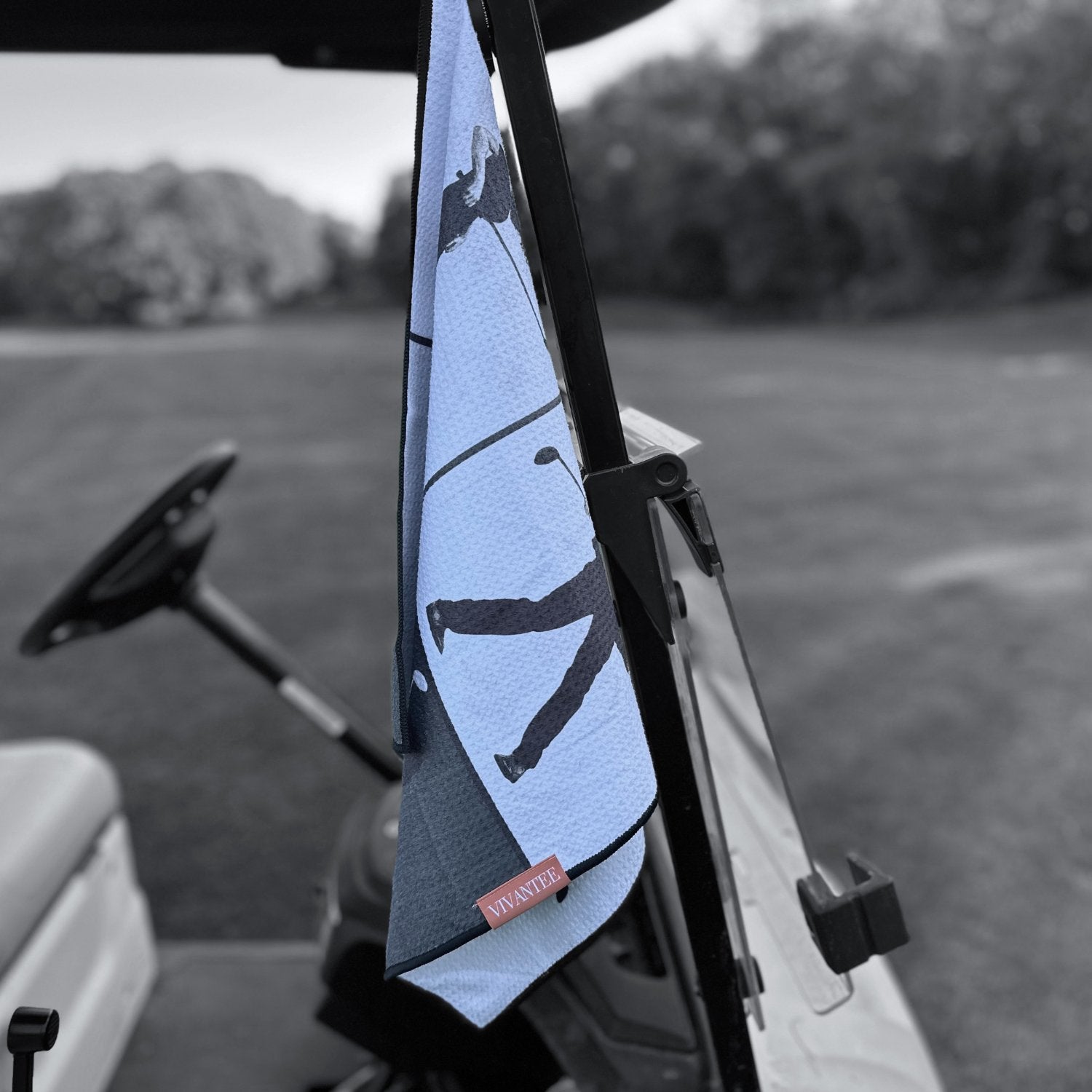 Magnetic golf towel in black and white attached to a golf cart with the golf course in the background.