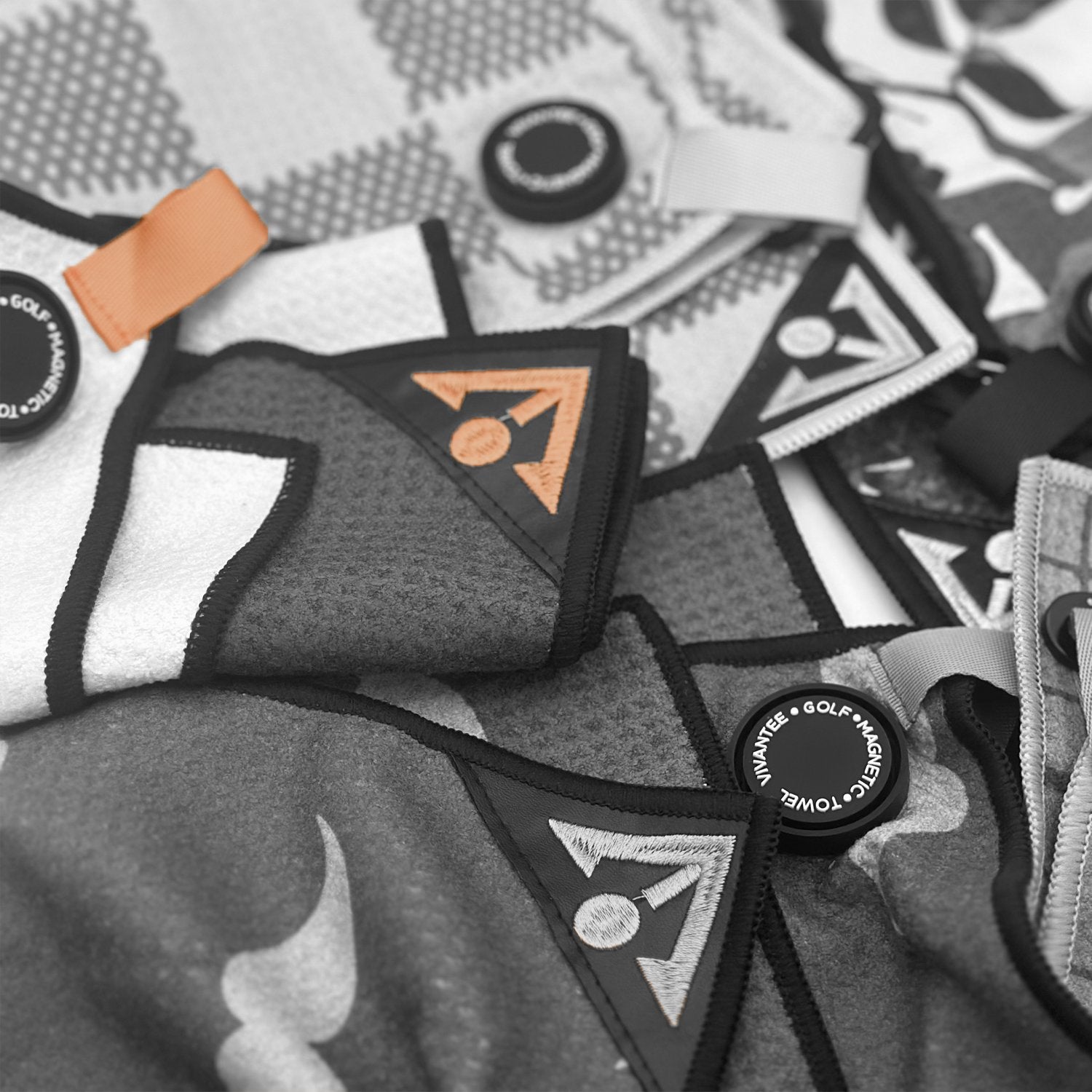 Zoomed in image of various VivanTee Golf magnetic golf towel designs showing the quality of our premium microfiber up close, image in black and white with pops of orange.