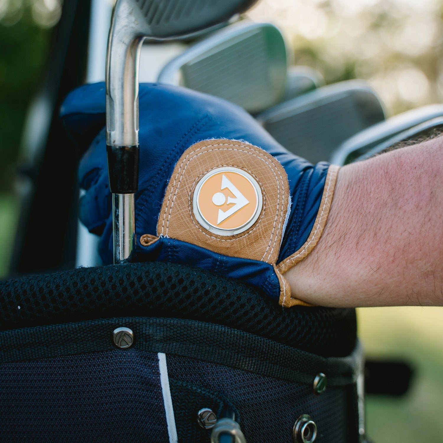 Close up of men's golf glove in midnight blue and brown resting their hand on their golf bag.