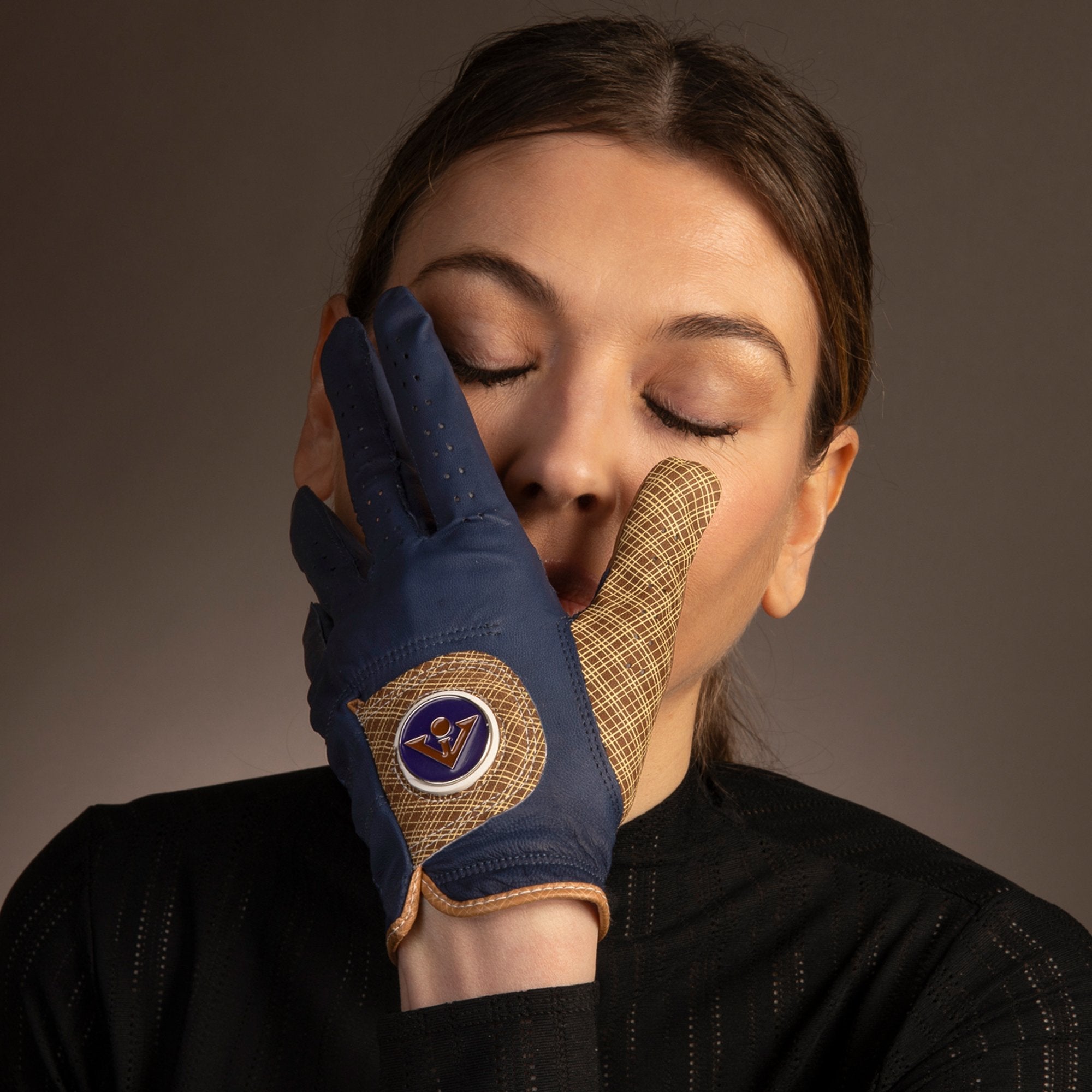 Woman with closed eyes touching her face with a navy blue leather golf glove, featuring a tan palm with a detailed mesh pattern and a vibrant VivanTee Logo.