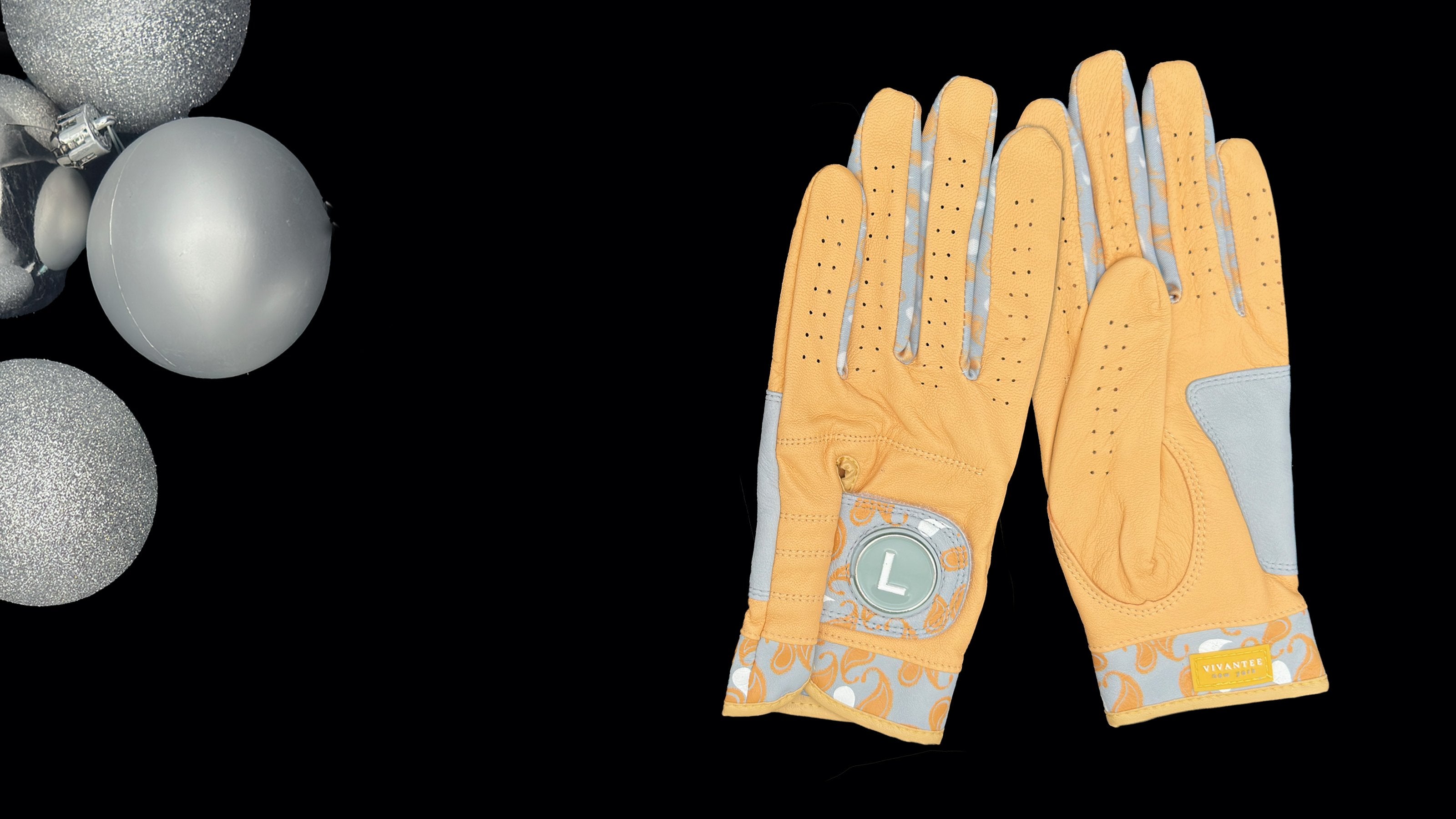 Pair of gold golf gloves with magnetic ball marker by VivanTee Golf on a black background and holiday ornaments.