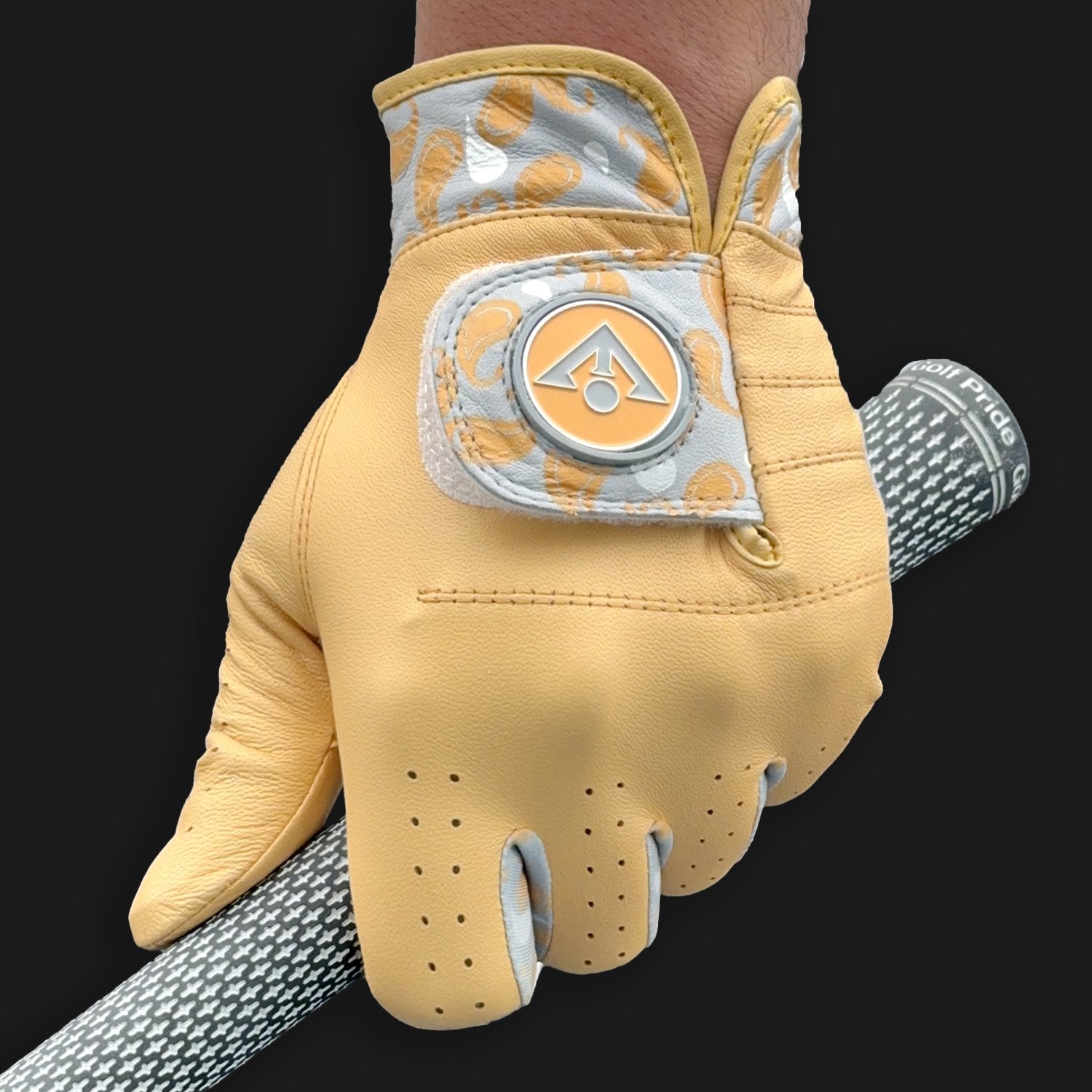 A cool Gold and grey golf glove with paisleys, holding a golf club with a dark background.