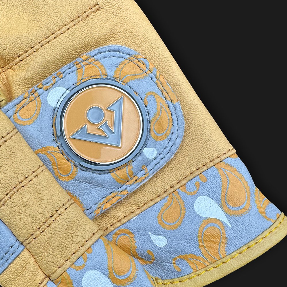 Close up of a golf glove with paisleys and a ball marker in gold, orange, and grey with a dark background.