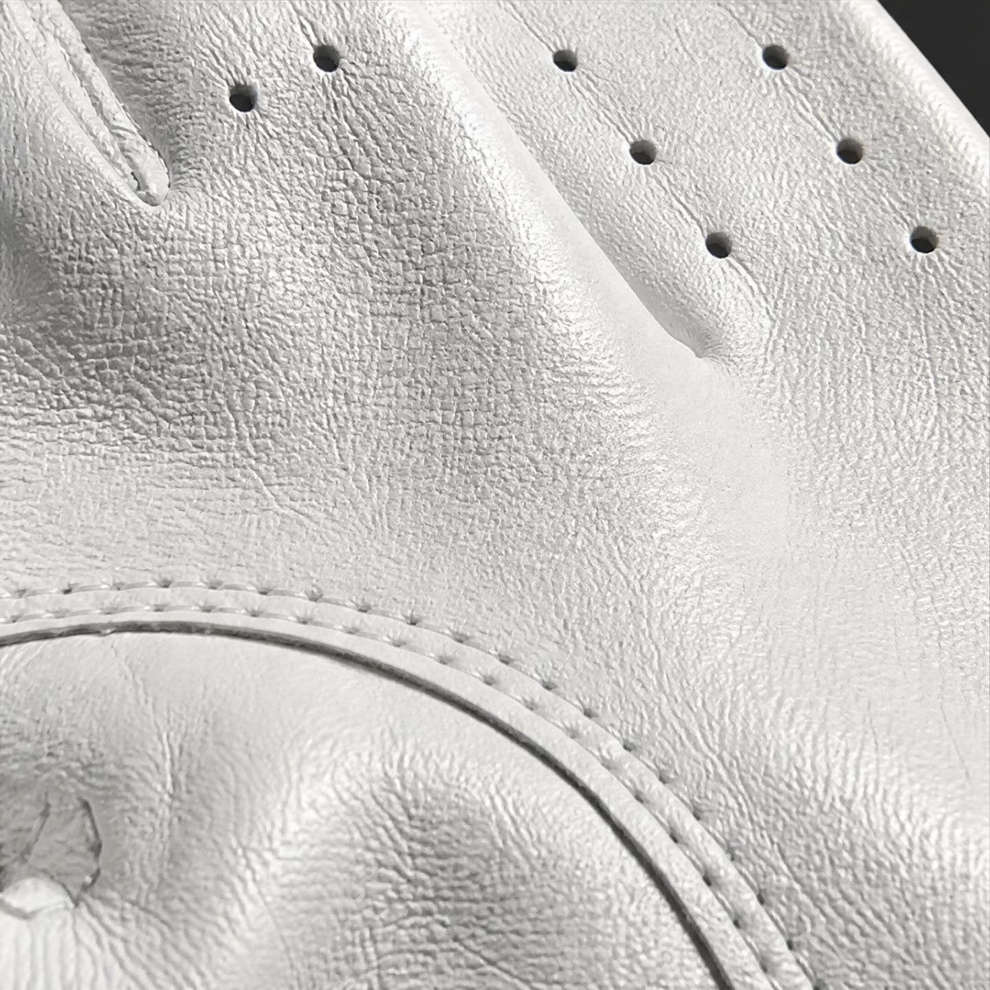 Close-up detail of a white leather golf glove showing the textured leather grain, perforations, and stitching.