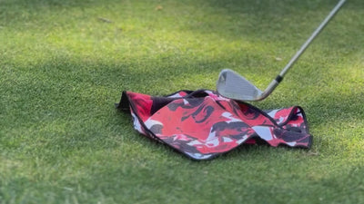 Video showing a red and black magnetic golf towel by VivanTee being picked up by a golf club on the ground.