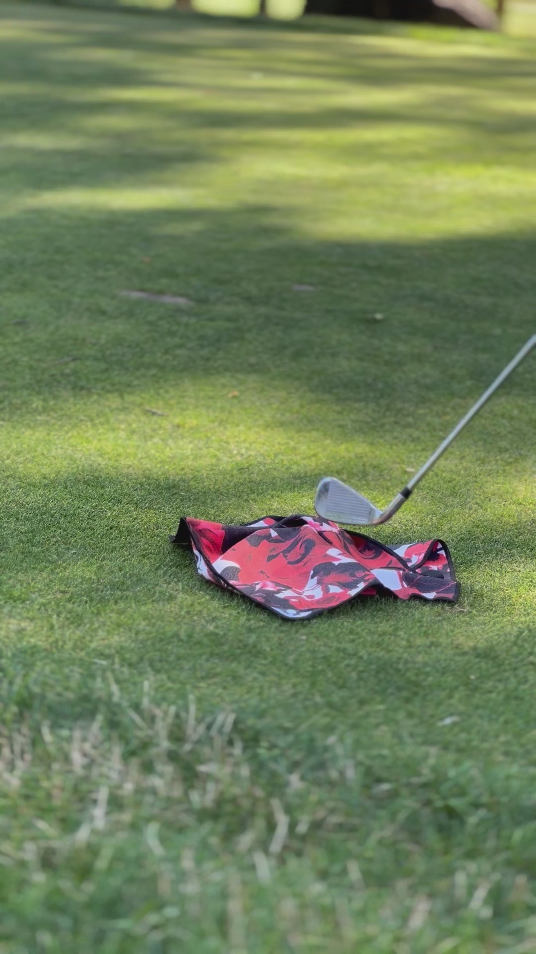 Video showing a red and black magnetic golf towel by VivanTee being picked up by a golf club on the ground.
