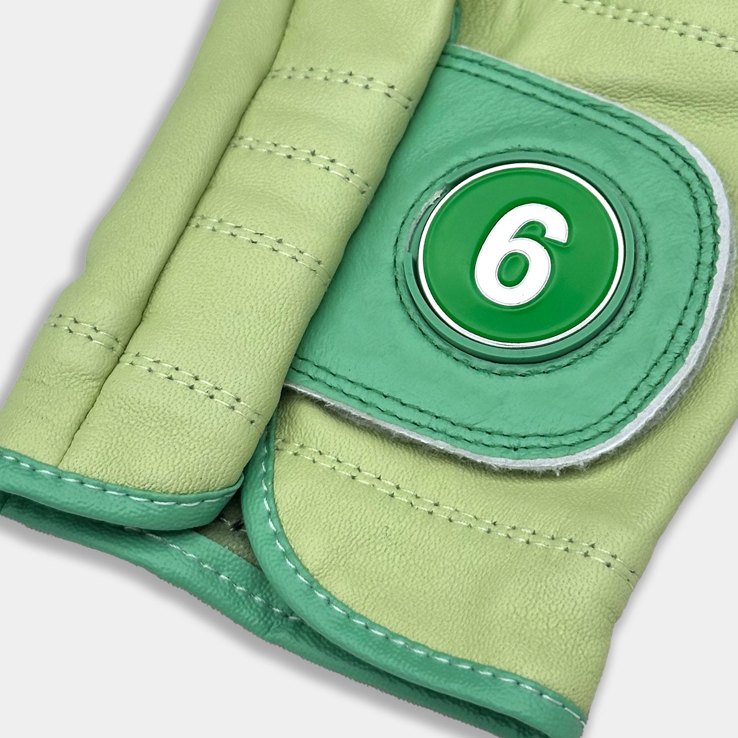Green golf glove with a 6 train magnetic ball marker close up with grey background.