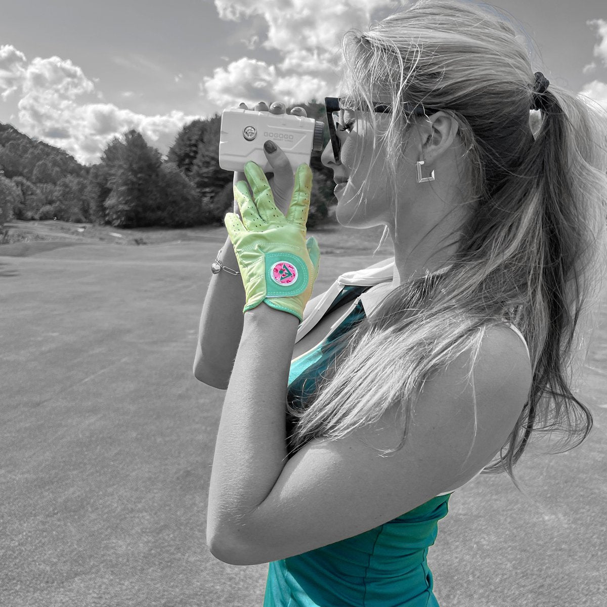 Women in a mint green fancy golf glove holding up a range finder in a green dress and a monochromatic setting. 
