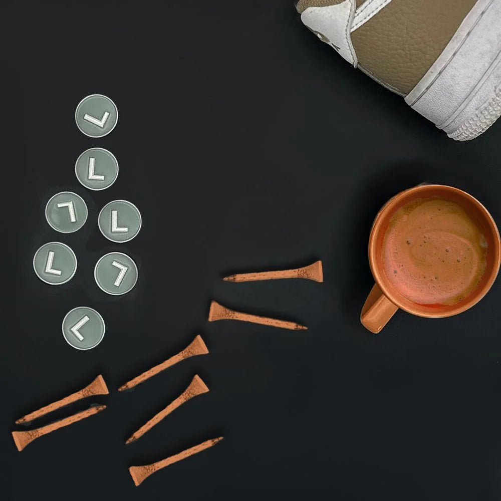 Subway ball marker collection for our magnetic golf gloves next to orange tees and a cup of coffee.