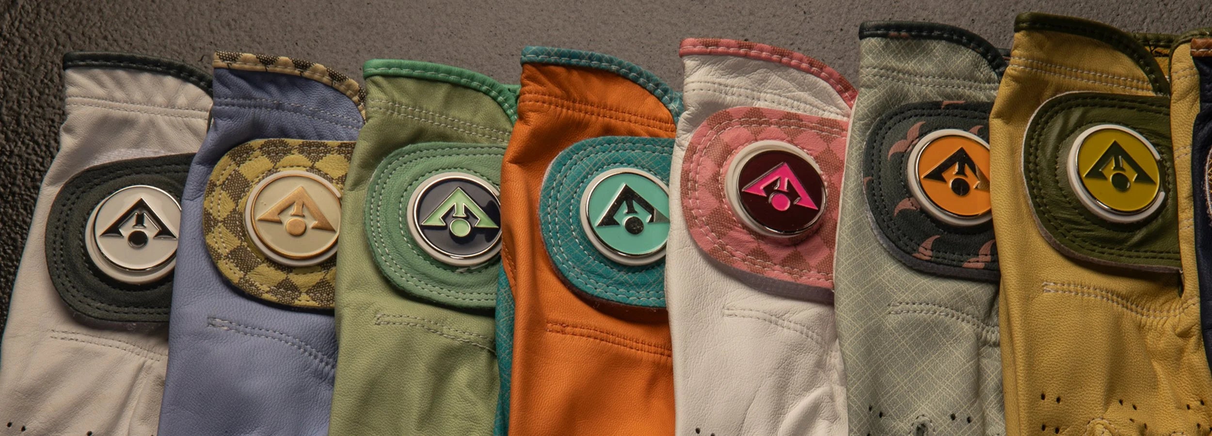 Unique golf gloves with ball markers laid out across each other in various colors and styles, showing the uniqueness of each design.