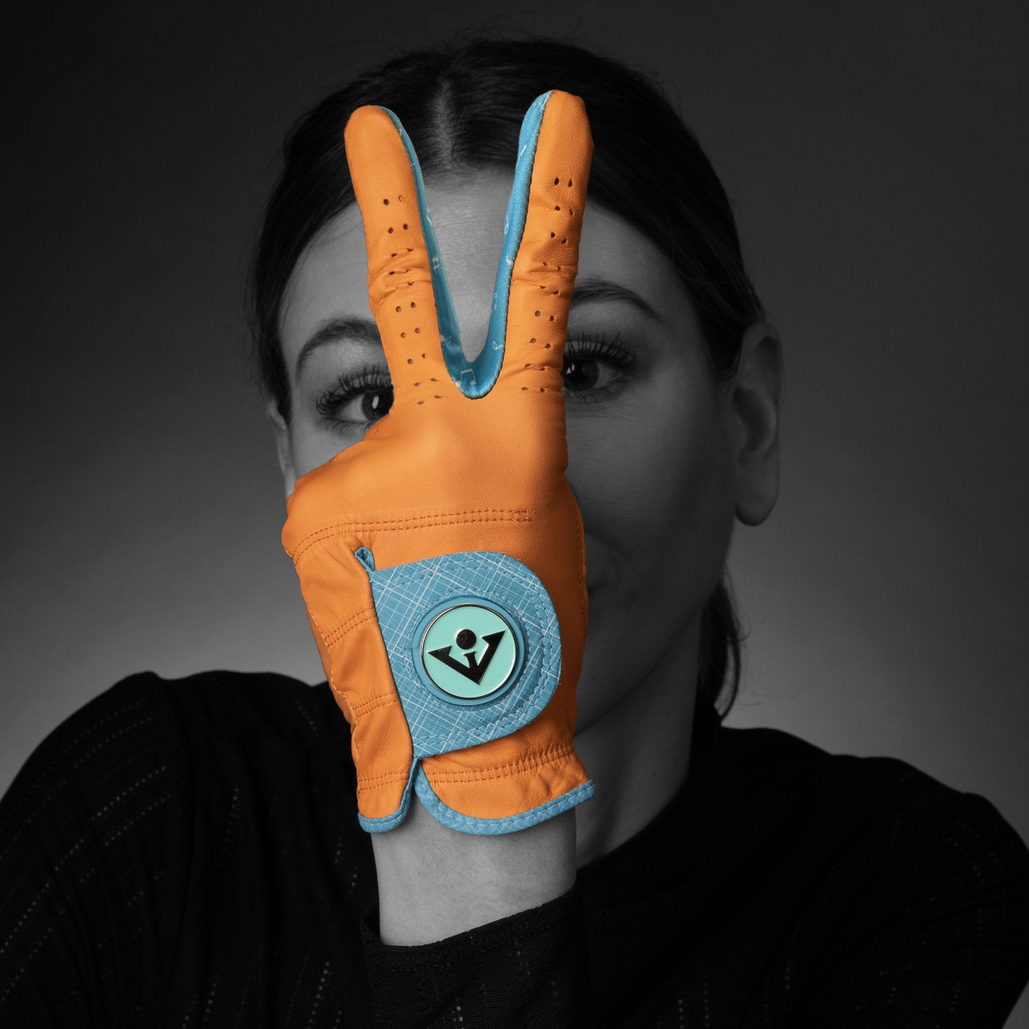 Woman wearing an orange golf glove with magnetic ball marker showing a peace sign in black and white.  