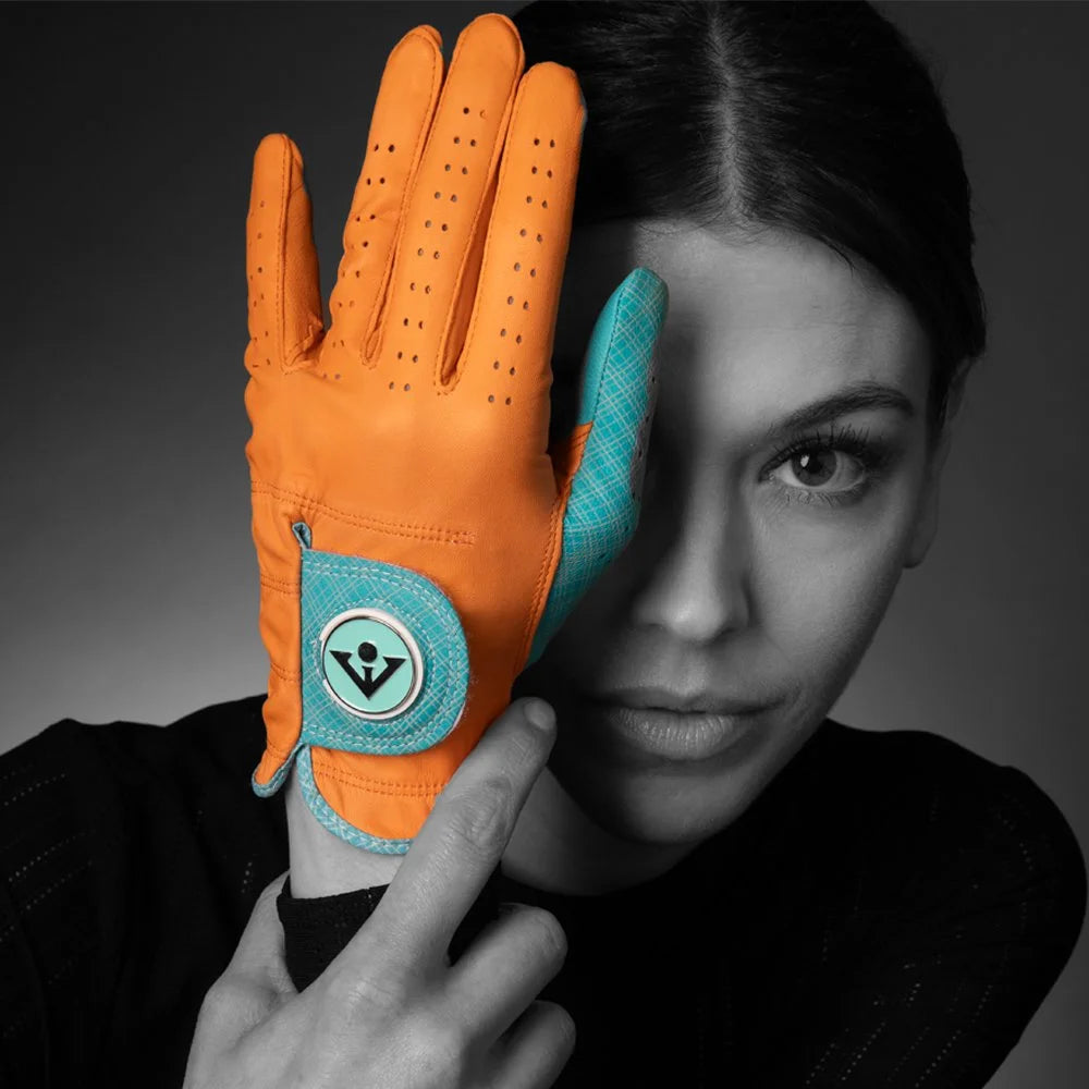 Orange women’s golf glove with ball marker in front of models left eye in black and white showing a vibrant color selection.