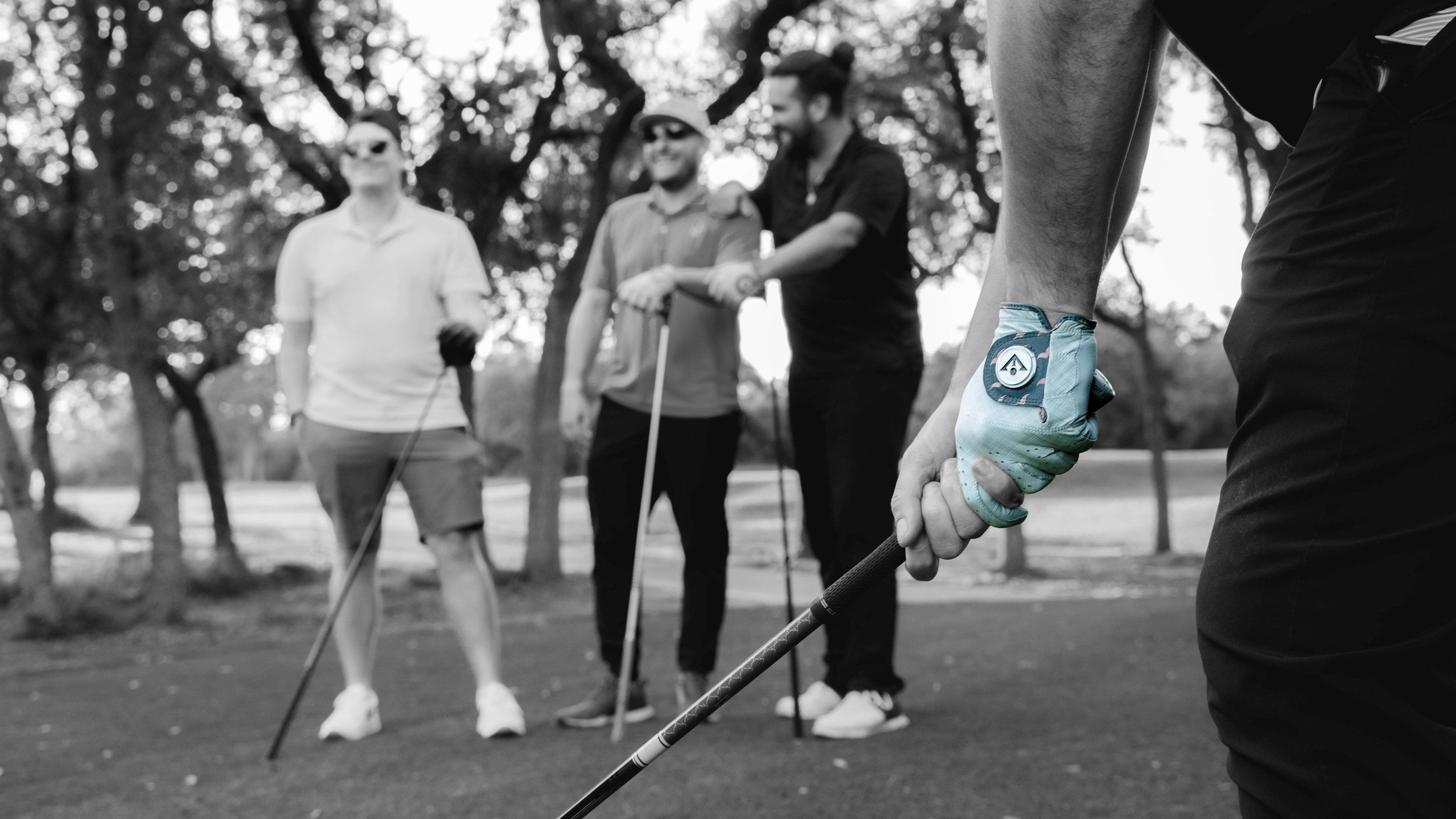 Person holding a golf club with a stylish golf glove, with two other people in the background laughing.  