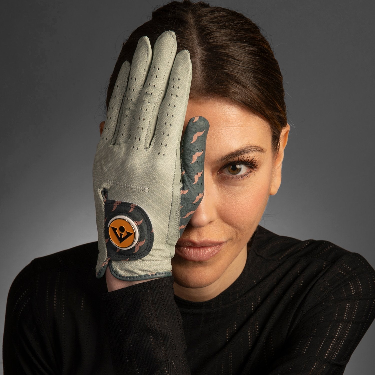VivanTee women's Mustache Patterned golf glove in front of a models right eye with a charcoal background.